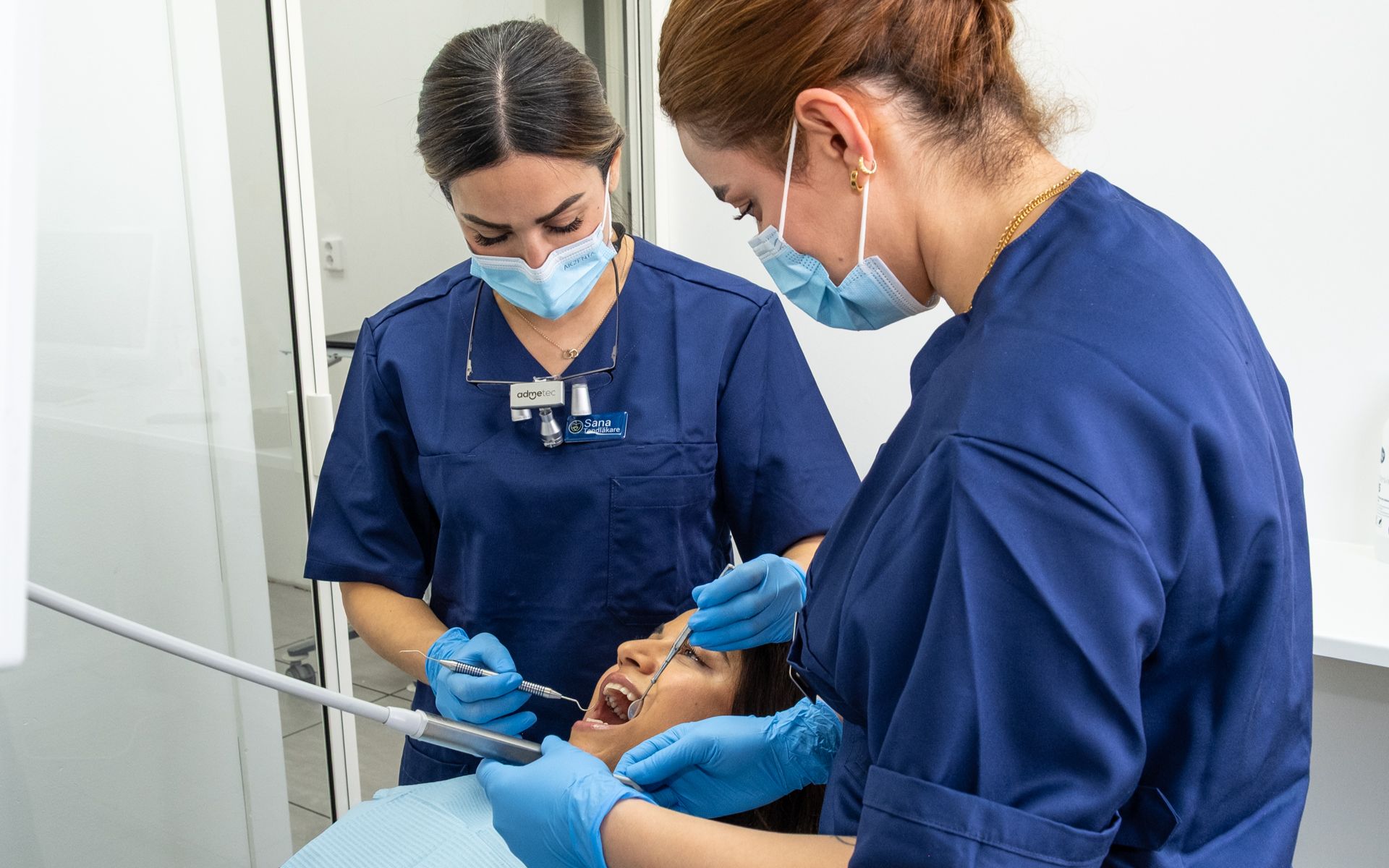 Två glada tandläkare ler brett mot kameran på Svea Dentals mottagning i Göteborg, redo att hjälpa med käkkirurgi och eftervård.